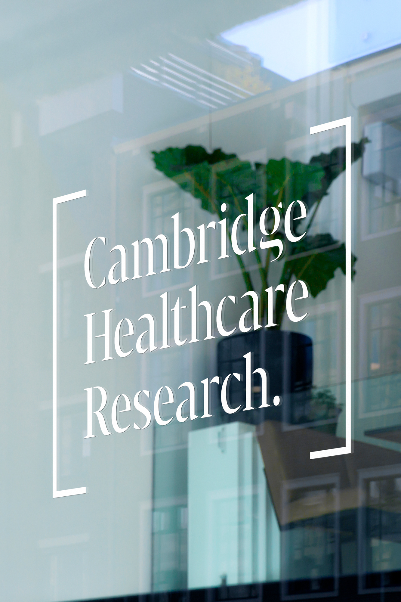Cambridge Healthcare Research signage on window with potted plant inside building, clear glass, building reflection, light, airy, modern.