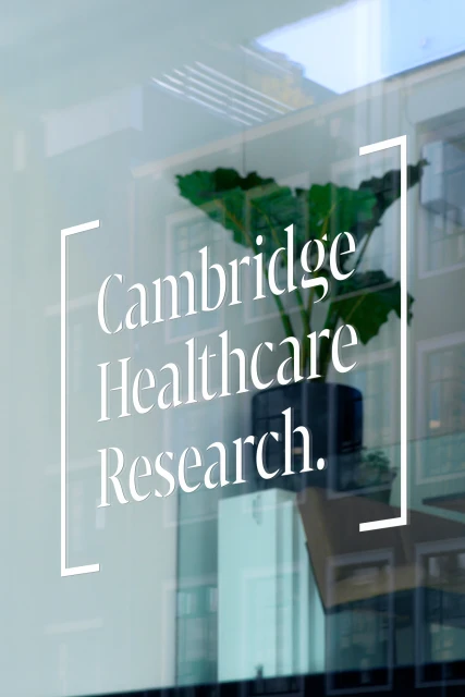 Cambridge Healthcare Research signage on window with potted plant inside building, clear glass, building reflection, light, airy, modern.