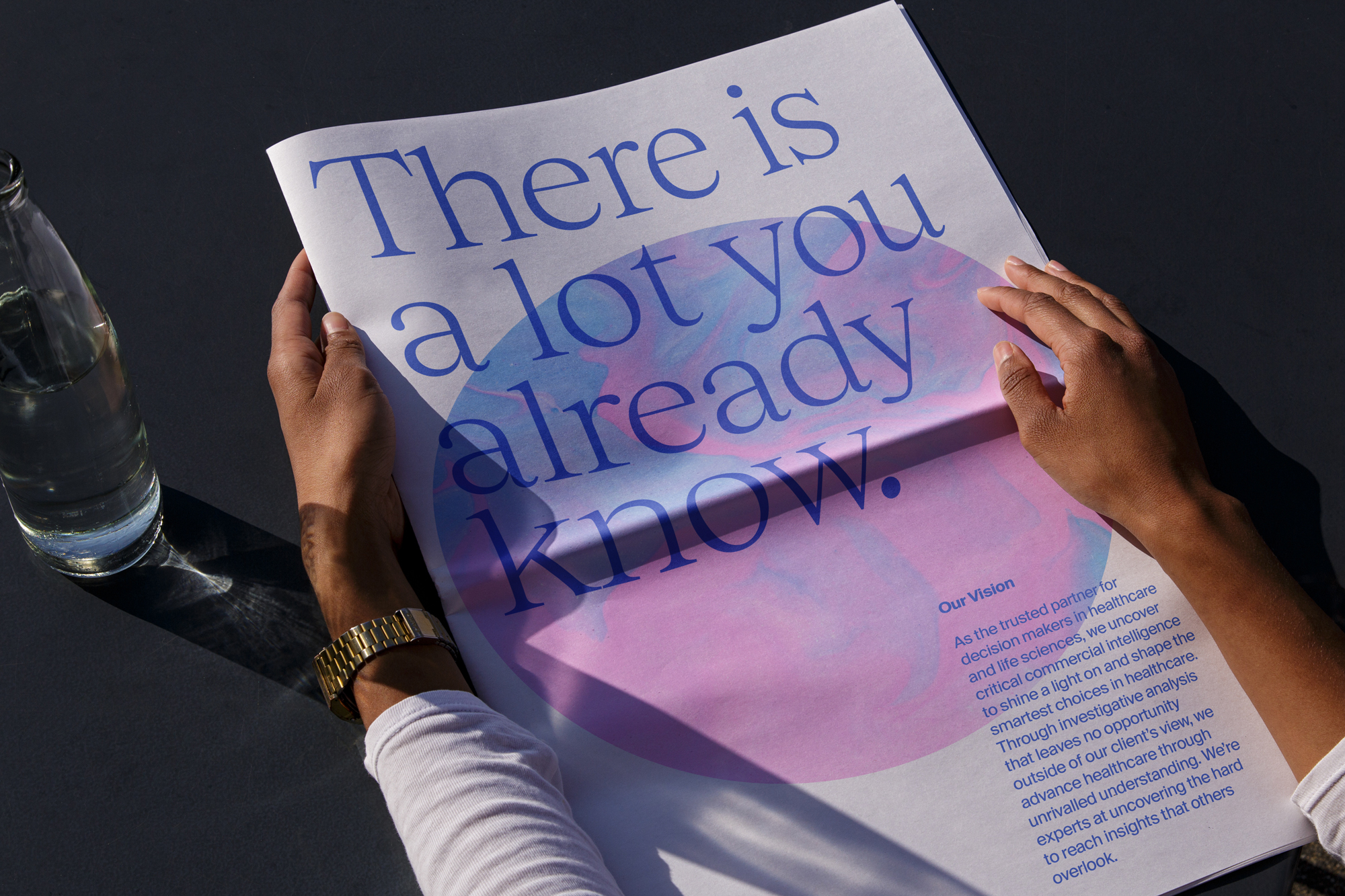 Hands holding newspaper with the text 'There is a lot you already know,' water bottle, and shadow on table. Healthcare ad.