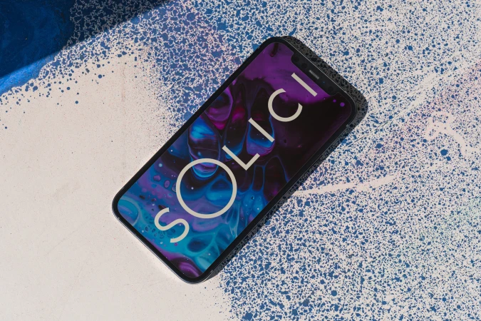 Modern smartphone displaying SOLICI branding on a purple and blue abstract background atop a splattered paint surface with dynamic shadow.