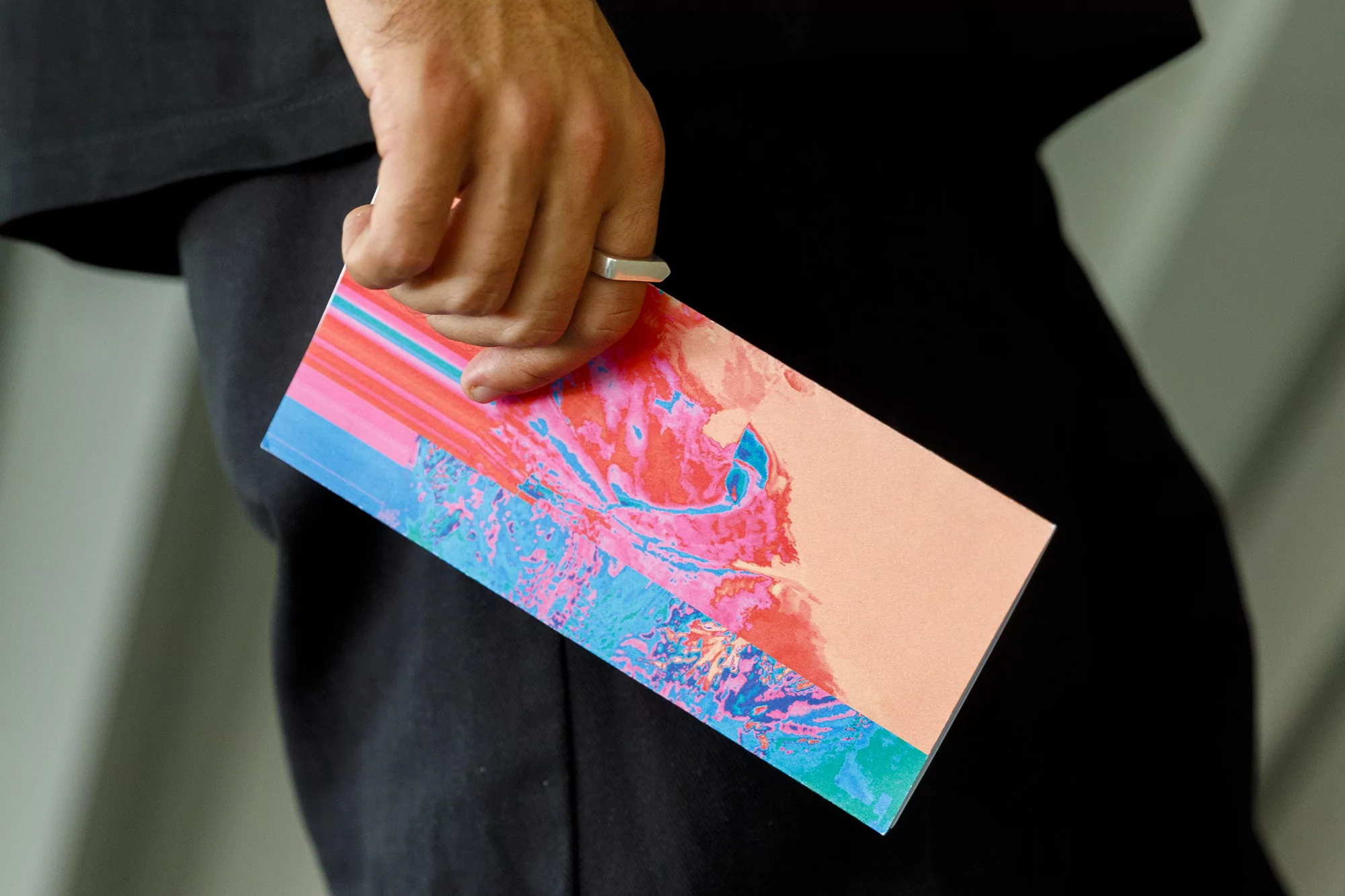 Close-up of a hand holding an abstract art print, featuring vibrant colors, modern design, and a stylish silver ring.