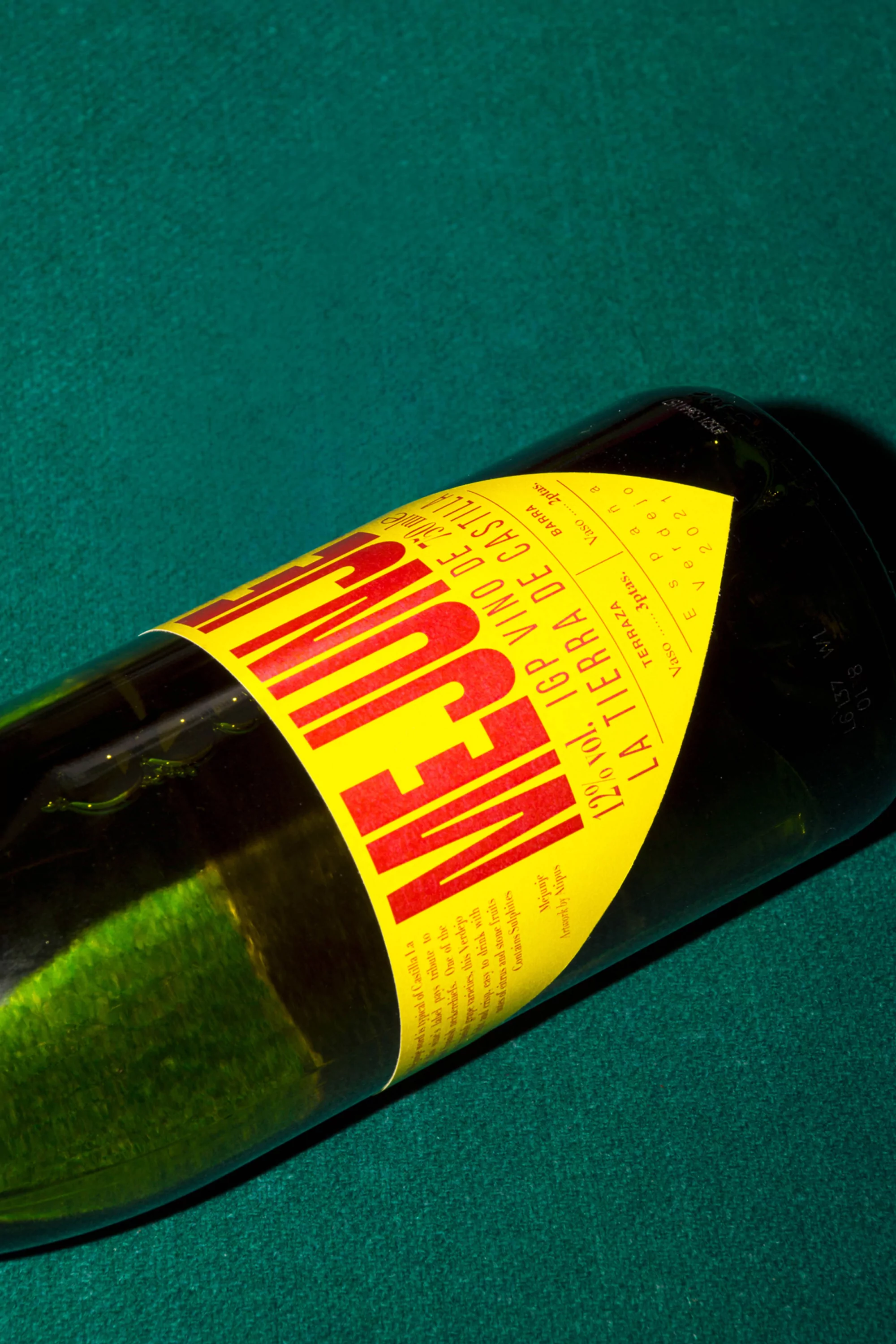 Close-up shot of a tilted green glass wine bottle with a yellow label and red text, on a green surface, creating a vibrant contrast.