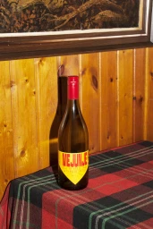 Wine bottle with yellow label and red cap on a tartan tablecloth against wood paneling