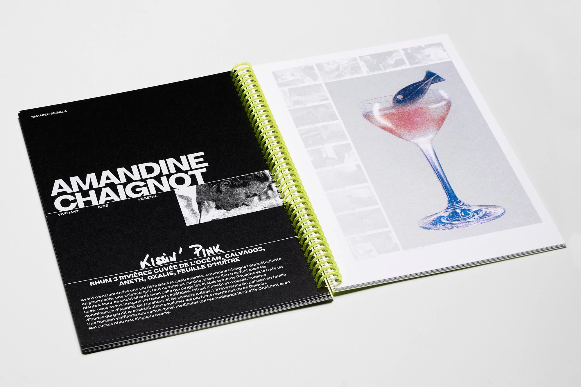 Open spiral-bound book featuring a cookbook page with a pink cocktail illustration and adjacent black page with chef's name.