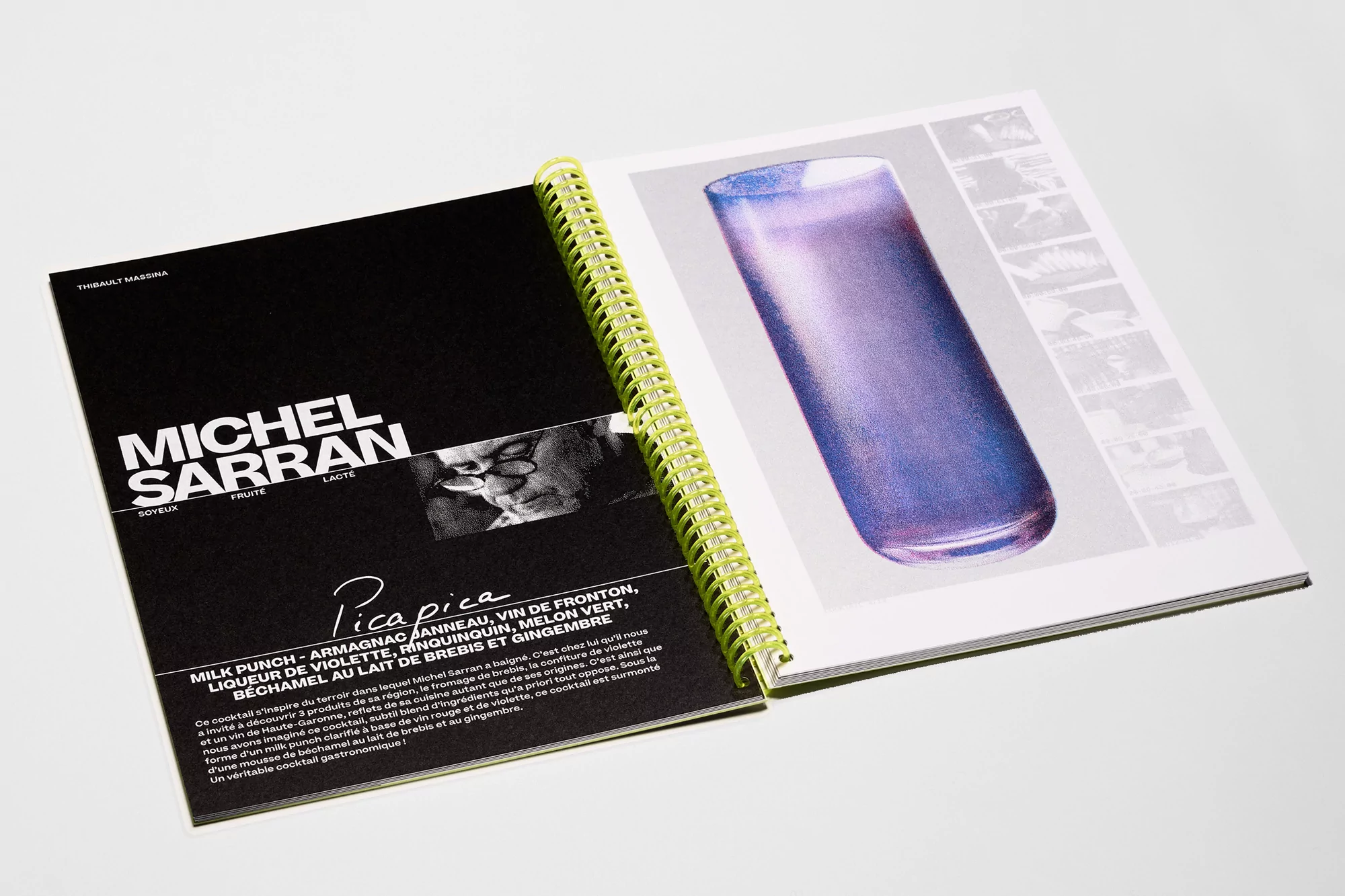 Open cookbook displays purple drink illustration with text overlay. Lime spiral binding is prominent. Cookbook rests on white surface.