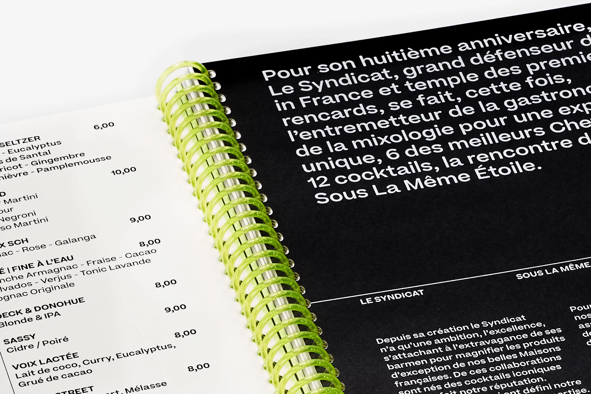 Close-up of a spiral-bound book featuring cocktail recipes in French, with a black and white color scheme, and a green spiral.