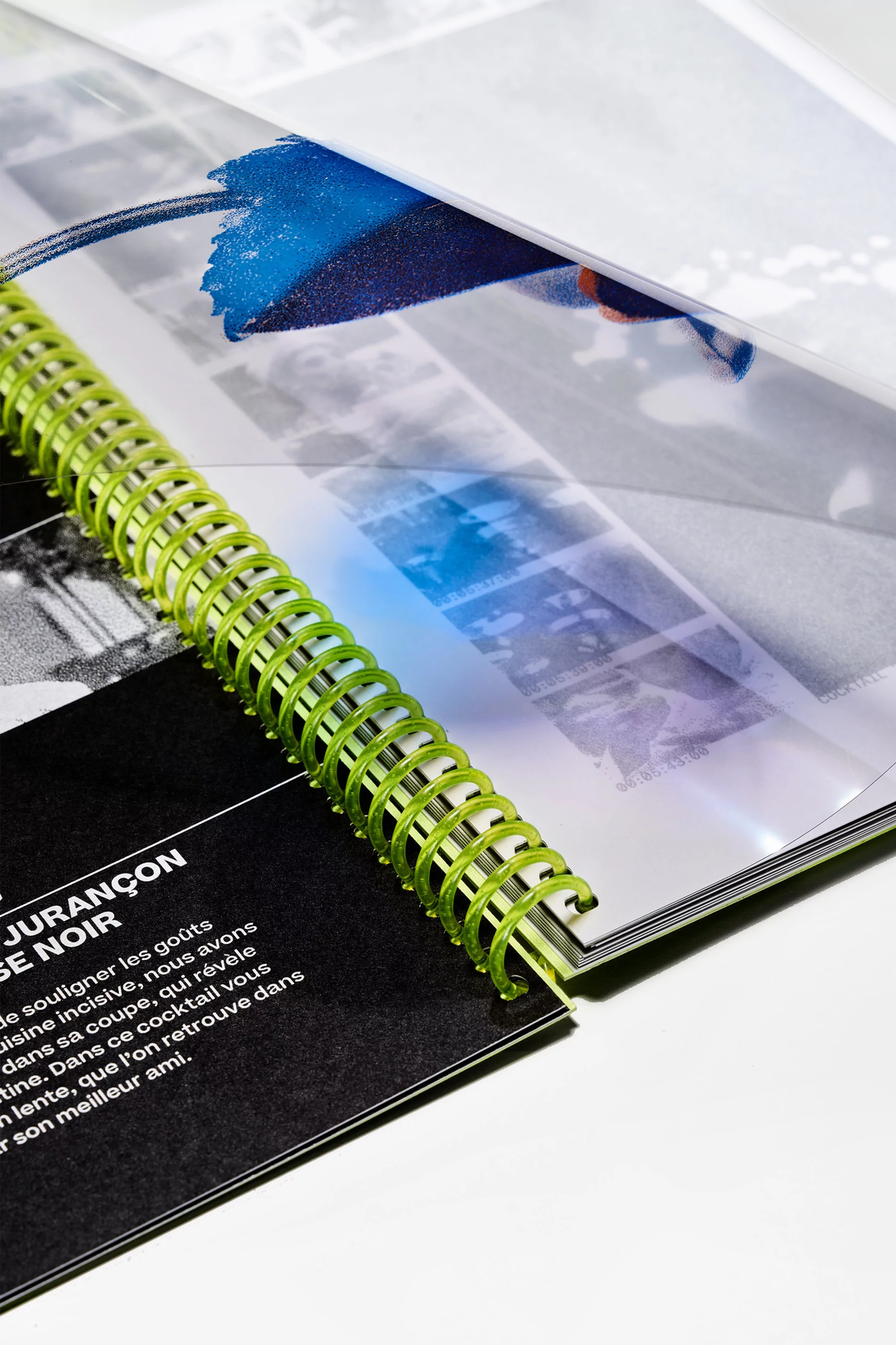 Open spiral-bound notebook with black text page and art image page, showcasing bright green spiral and clear protector sheet.