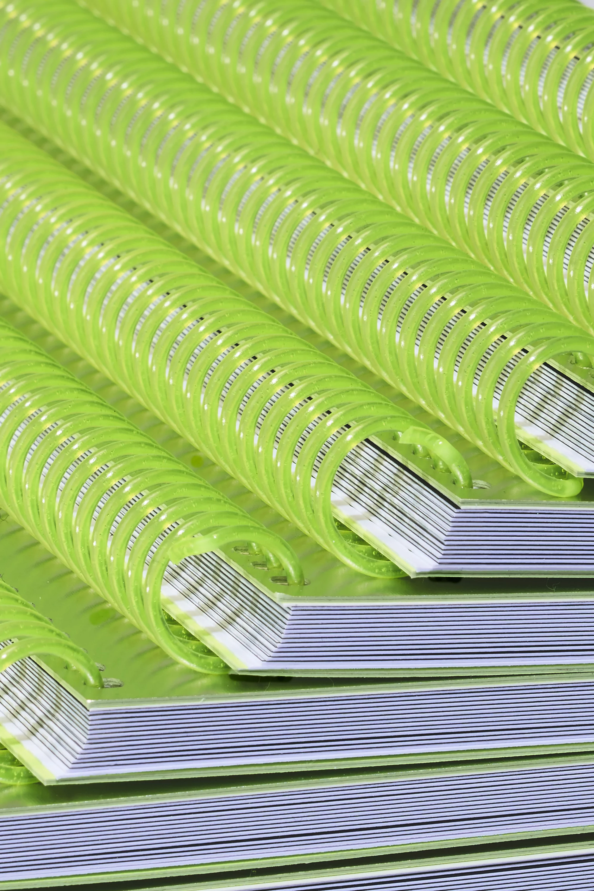 Close-up on a stack of notebooks featuring a spiral binding made of light green plastic. The notebooks are stacked, creating a pattern.