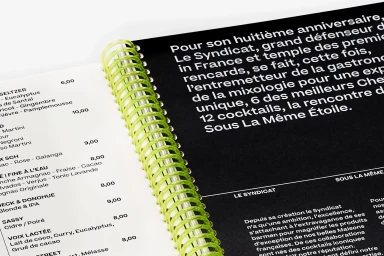 Close-up of a cocktail menu booklet bound with a vibrant lime green plastic spiral spine against a white background.