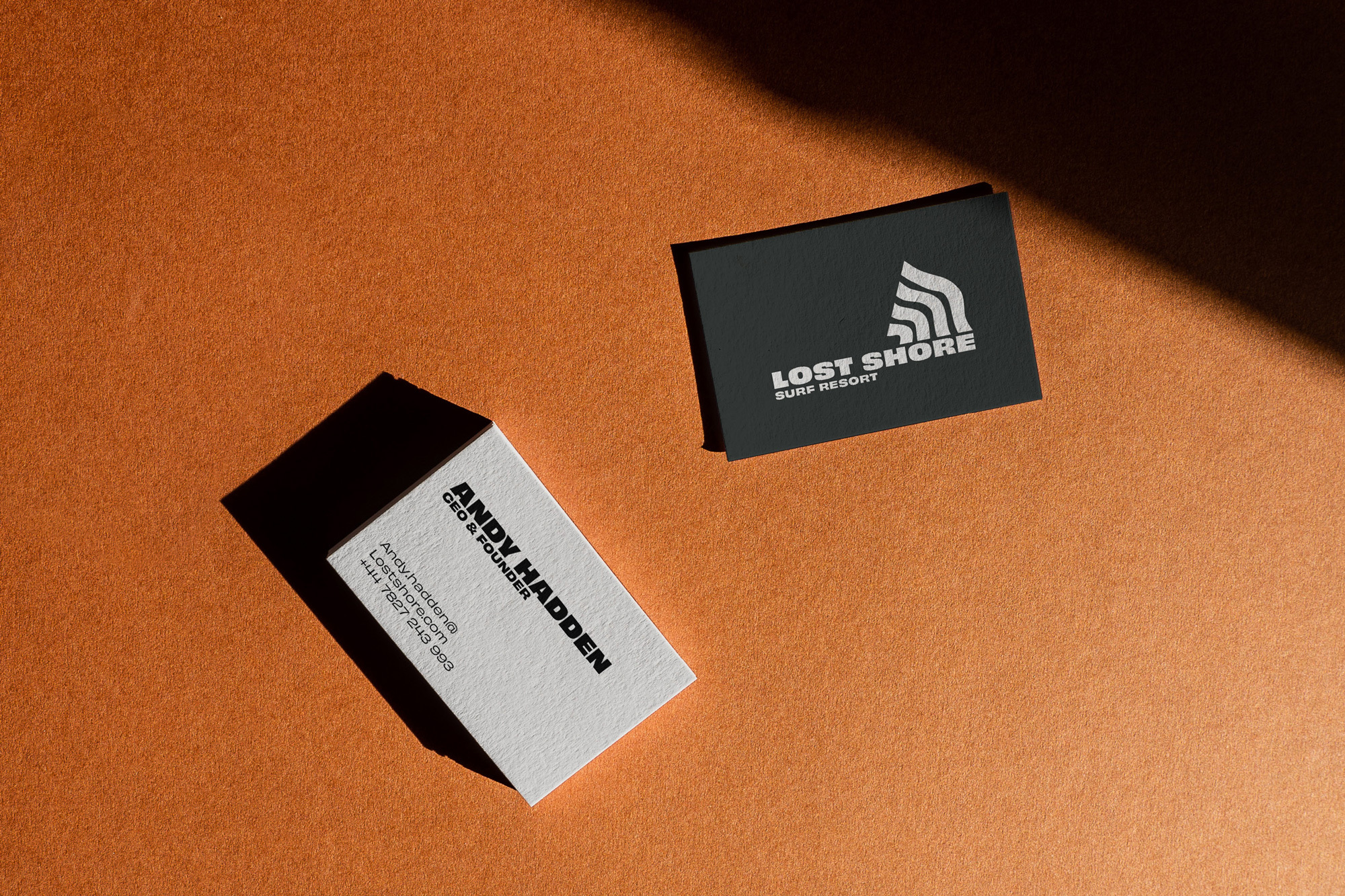 Two business cards, one white for Andy Hadden CEO & Founder, one black for Lost Shore Surf Resort, on a textured orange surface.