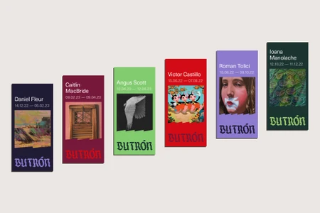 Six colorful vertical exhibition posters featuring artist names and dates arranged diagonally on a light grey wall.