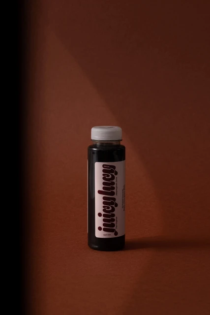 Juicy Lucy beverage bottle on brown backdrop, showcasing minimalist product presentation with contrasting shadows, ideal for food & beverage promotions.