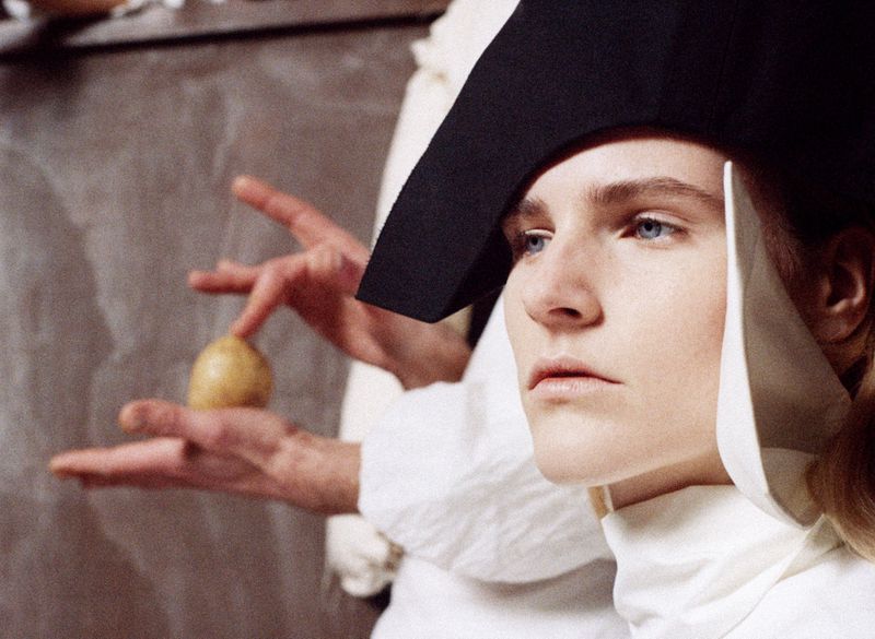 Woman with blue eyes wearing a black and white headpiece holds a potato in her hand in a close-up studio shot.