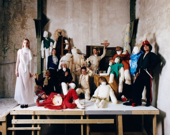 Group of people and mannequins posed on a platform in a room with distressed walls, creating a surreal and artistic composition.