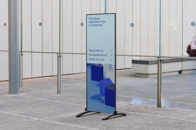 Vertical digital signage display on a modern concrete plaza featuring Evidi branding and event schedule details.