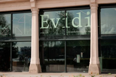 Storefront exterior with large glass windows featuring bold Evidi branding typography and neoclassical columns.