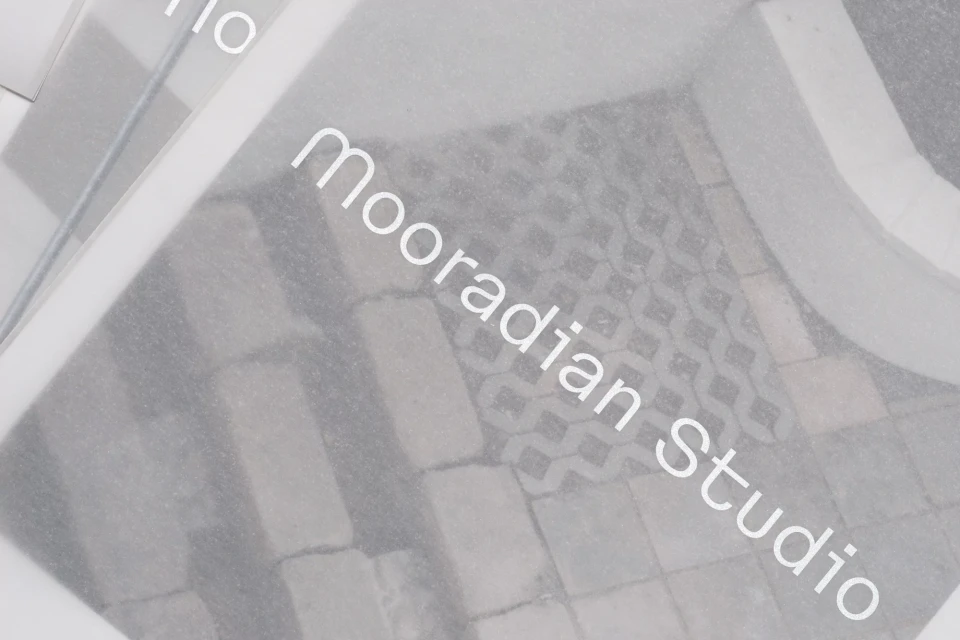 Close-up of a patterned brick floor, partially obscured by sheets of translucent vellum, featuring the text 'Mooradian Studio'.