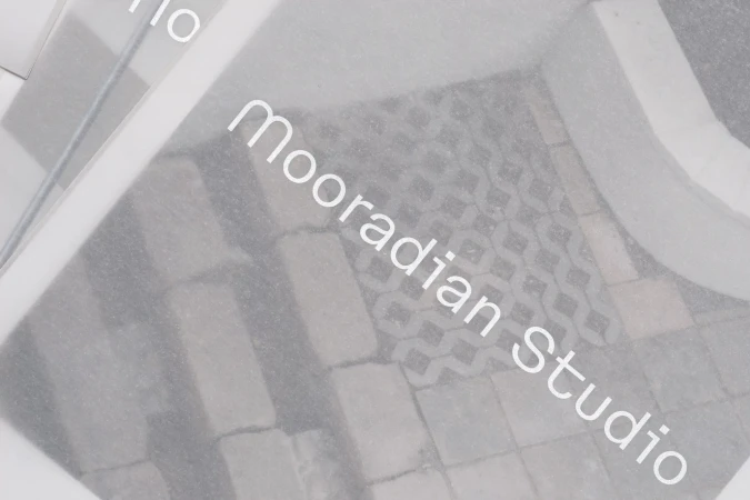 Close-up of translucent frosted paper overlaying textured stone pavers with the text mooradian studio printed clearly on top