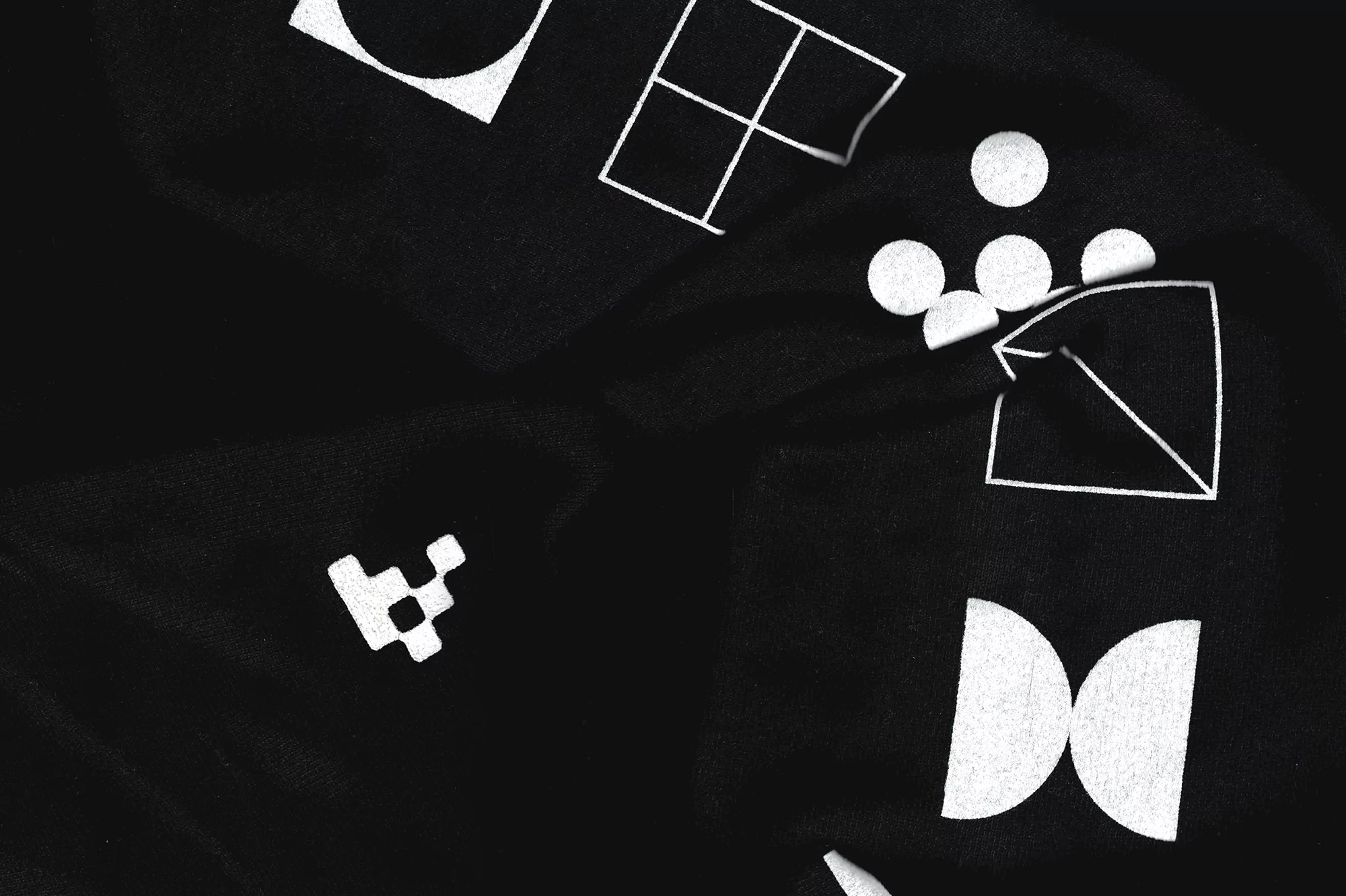 Black fabric background with scattered white geometric shapes including circles, squares, triangles, and other abstract designs.