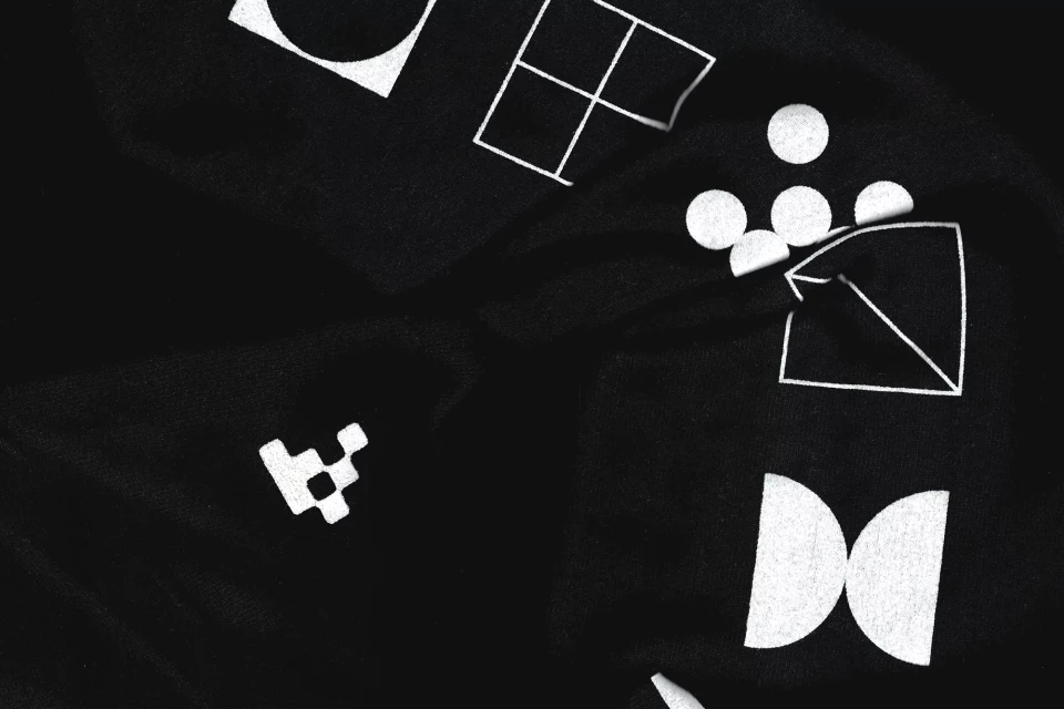 Black fabric background with scattered white geometric shapes including circles, squares, triangles, and other abstract designs.