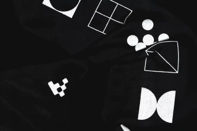 Close-up black fabric texture featuring various white geometric shapes and symbols printed across the folded material surface.