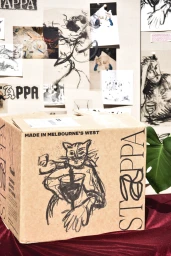 Cardboard shipping box with illustrated cat artwork and typography for Stappa resting on a burgundy velvet surface.