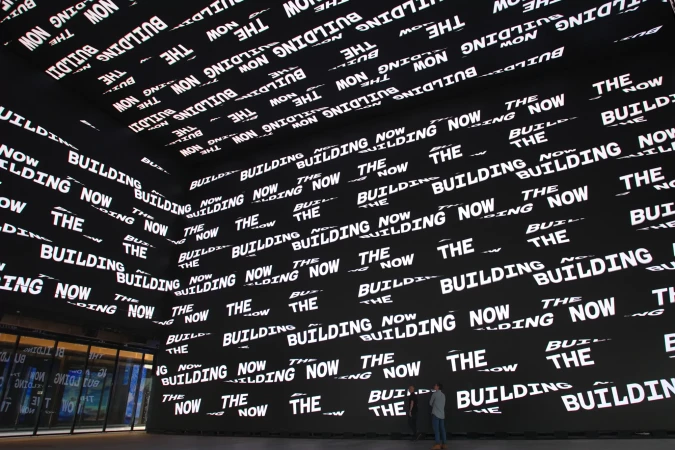 Indoor architectural view of two people standing in a large room with walls covered in black and white text art.