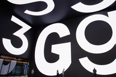 Giant glowing white typographic letters on large black curved screens inside a building with people standing below