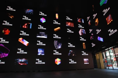Massive indoor digital screen wall displaying media grids and The Now Building text for Outernet brand identity