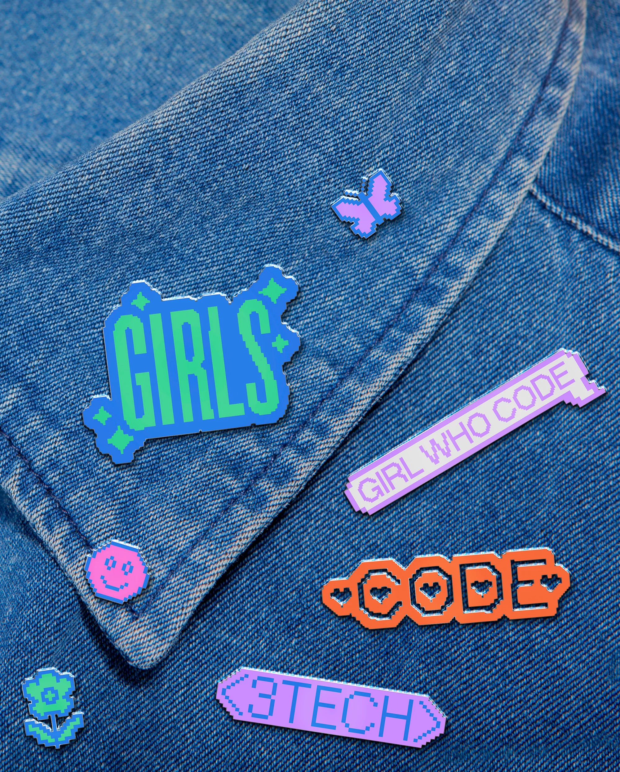 Denim jacket with pixelated and colorful pins and patches including images and text 'Girls who code', 'Code' and '3Tech'.