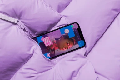 A smartphone tucked into a light purple puffy jacket pocket displaying a graphic interface with a portrait.