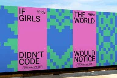 Large outdoor banner with pink panels featuring bold black typography reading if girls didn't code the world would notice next to pixelated blue and green geometric patterns.