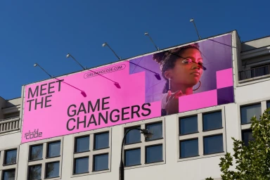 Large pink and purple Girls Who Code billboard reading Meet the Game Changers mounted on a light-colored urban building exterior