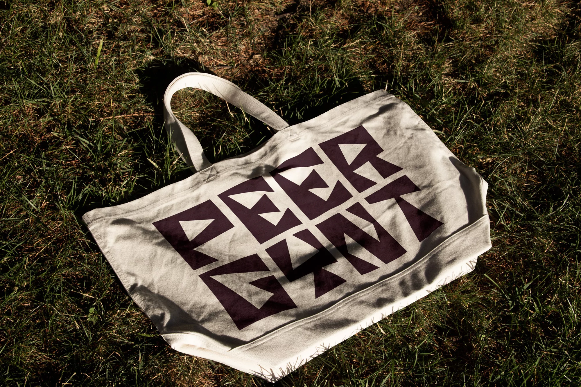 Tote bag featuring a geometric pattern and the text 'PEER GYNT' on grassy lawn, bathed in sunlight.