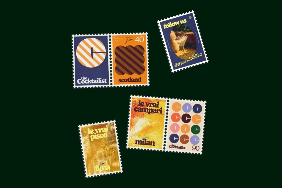 Collection of six The Cocktailist postage stamps with drink illustrations and retro designs on a dark green background in an overhead shot.