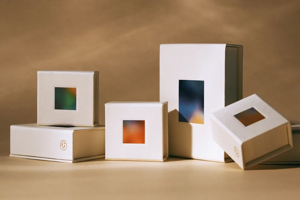 Arrangement of square white boxes with color gradient square cutouts on a tan surface. Product packaging for cosmetics or technology.