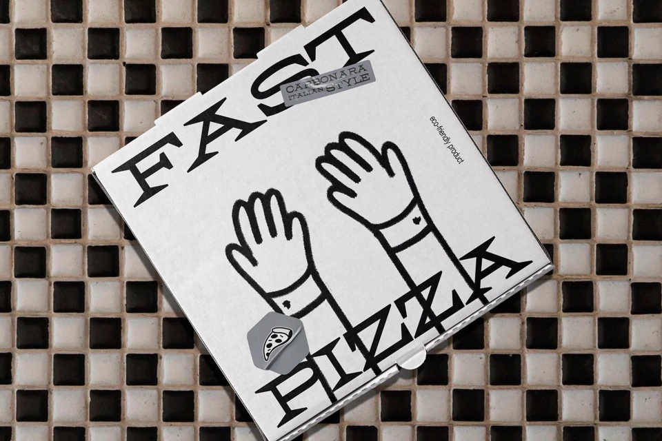 Overhead shot of a closed pizza box on a black and white tiled surface. The box is white with black hand illustrations.