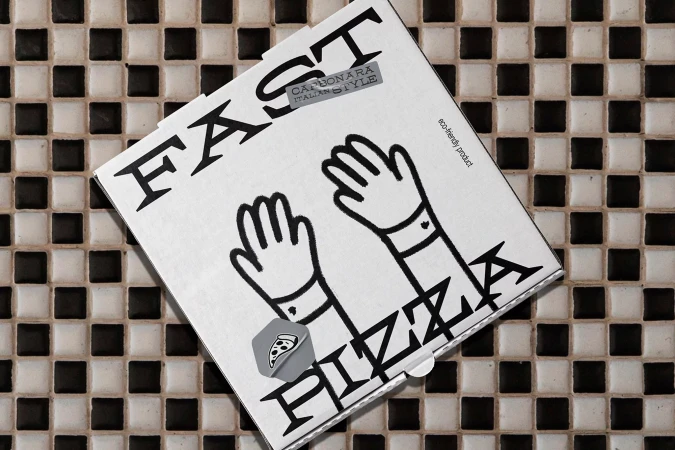 Overhead shot of a closed pizza box on a black and white tiled surface. The box is white with black hand illustrations.