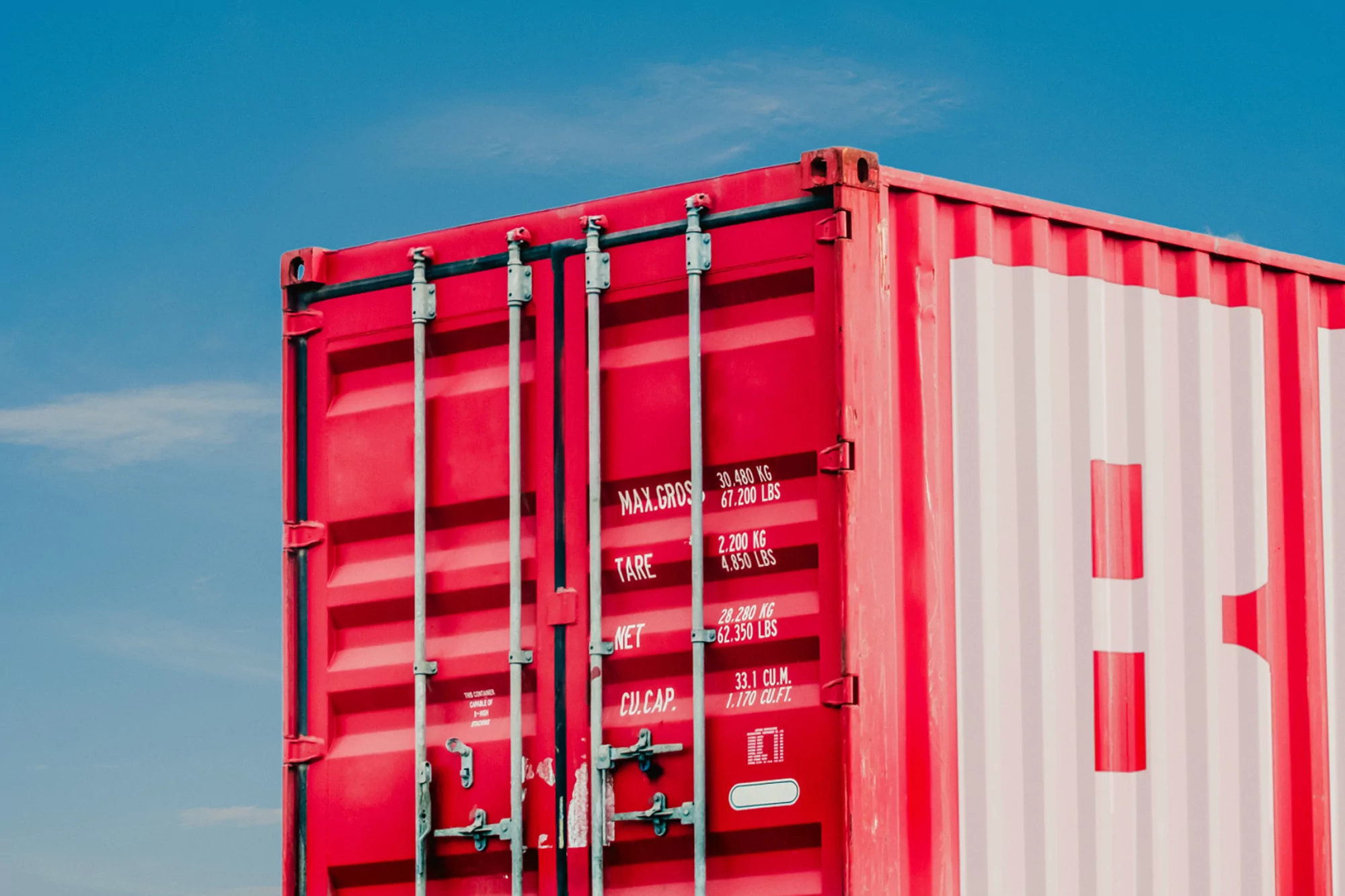 A red shipping container is set against a clear blue sky, showcasing the container's details and its scale within the outdoor setting.