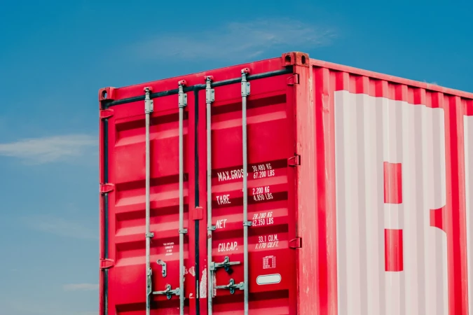 A red shipping container is set against a clear blue sky, showcasing the container's details and its scale within the outdoor setting.