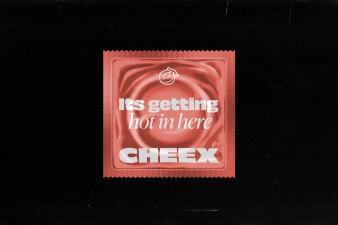 A single Cheex brand condom packet with white text on a peach background, centered on a black backdrop, intimate wellness advertising.