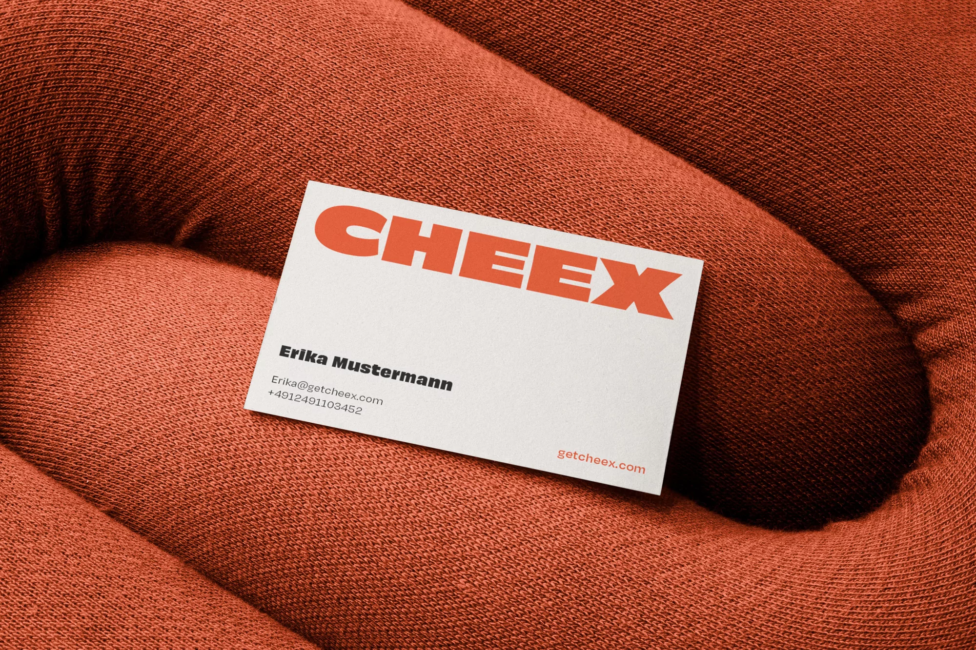 Close-up of a business card on textured orange fabric. The card displays the name CHEEX and contact information.