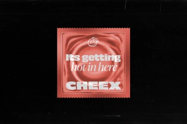 Red foil condom packet on a black background featuring white typographic brand identity design for CHEEX
