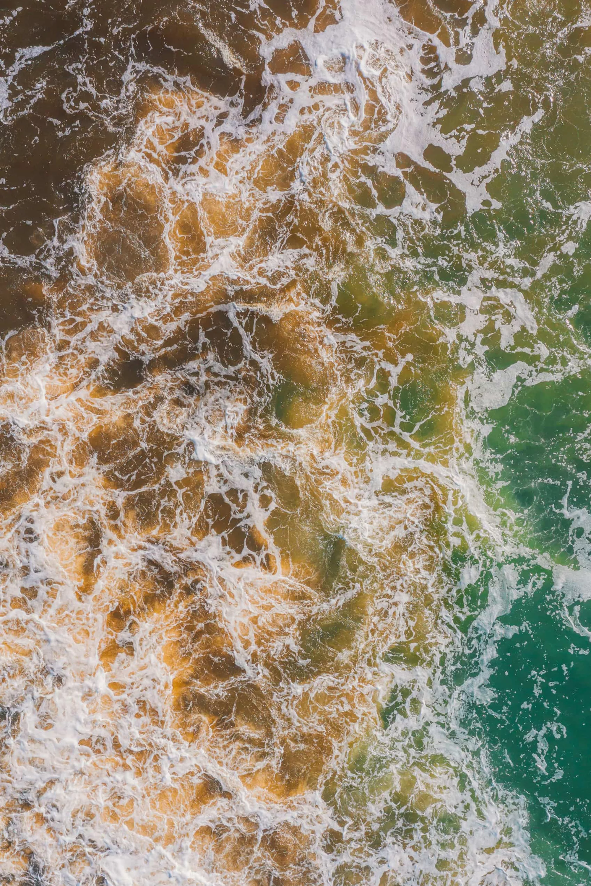 Aerial view of ocean water with brown and green algae swirls and sea foam creating a textured surface pattern.