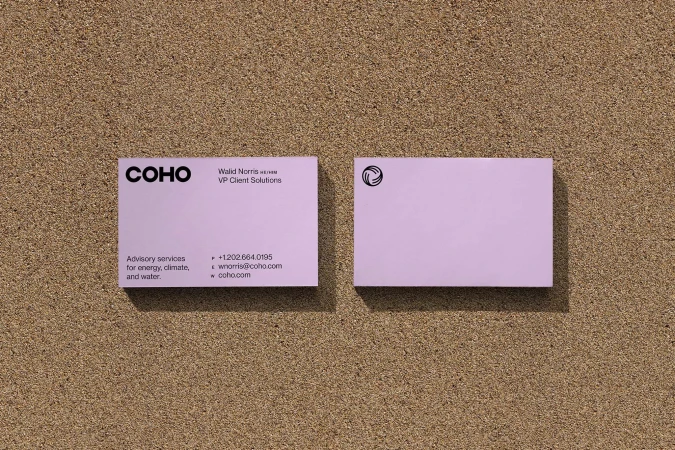 Two lavender business cards with the COHO logo and contact information arranged on a textured brown surface in a studio setting.