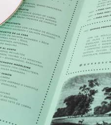Close-up angled shot of a printed menu on mint green paper with black typography and an engraved landscape illustration.