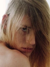 Close-up portrait of a person with long blonde hair partially covering their face, looking back over their shoulder