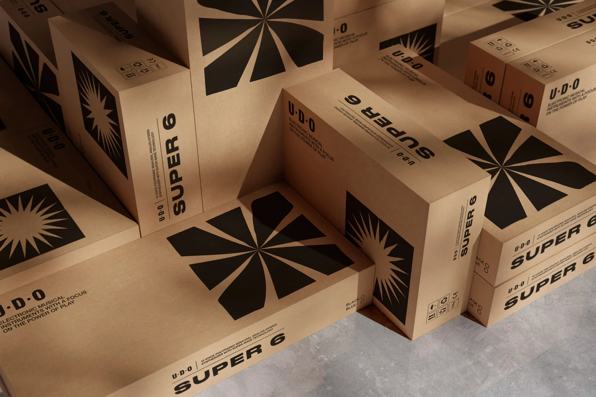 Boxes of UDO Super 6 musical instruments are stacked together, featuring black geometric designs and brand text on kraft paper.
