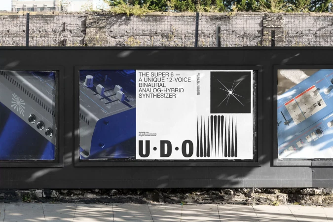 Outdoor posters advertise UDO Super 6 synthesizer, displayed on a weathered stone wall along a city sidewalk.
