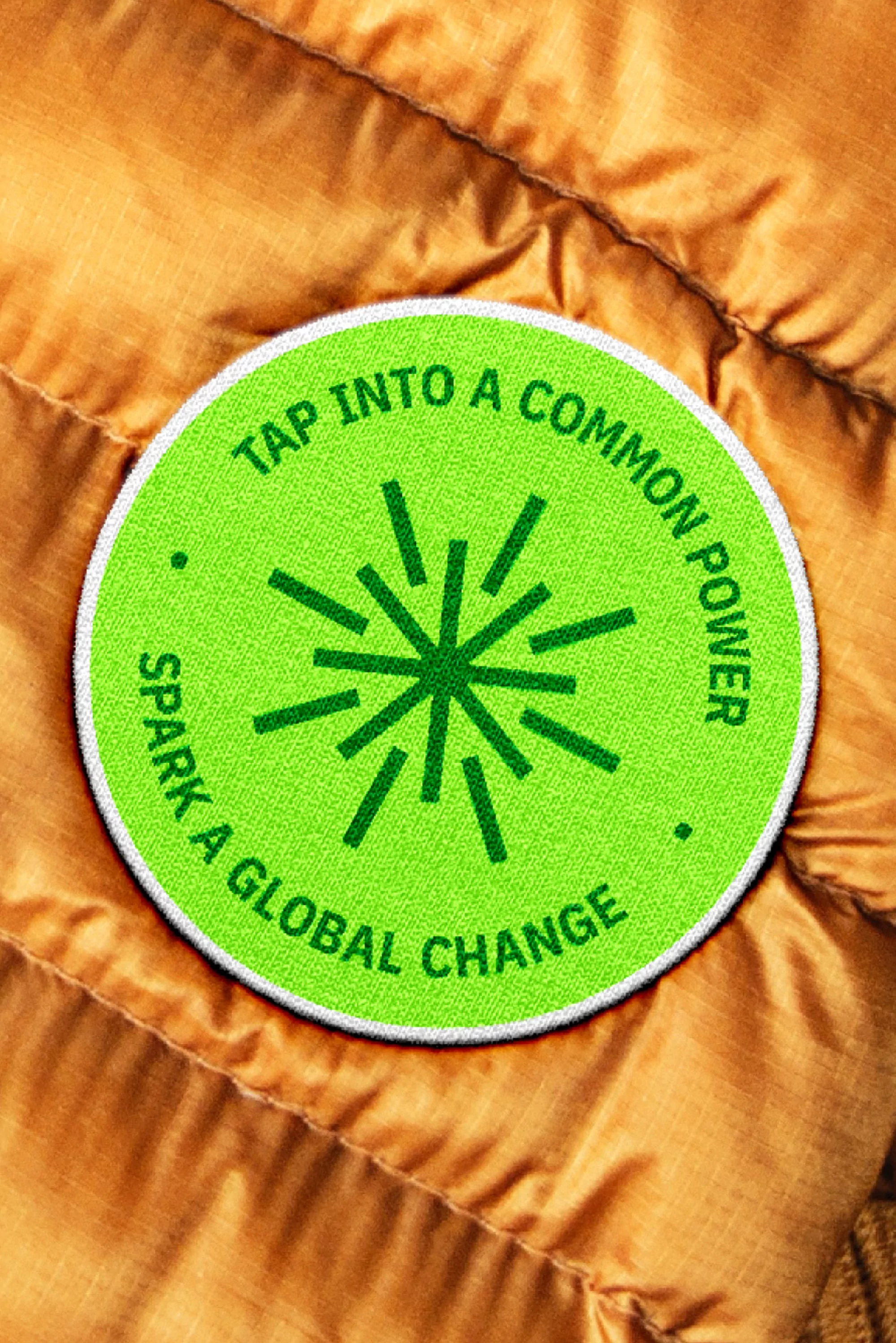 Close-up of a green circular patch with the text 'Tap Into a Common Power' and 'Spark a Global Change' on gold colored jacket.